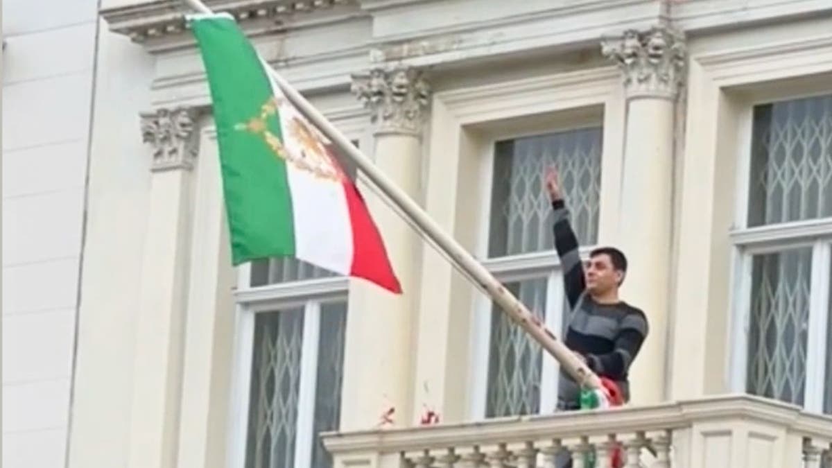 Protester scales Iranian Embassy in London, tears down regime flag, hoists pre-revolution symbol at george magazine