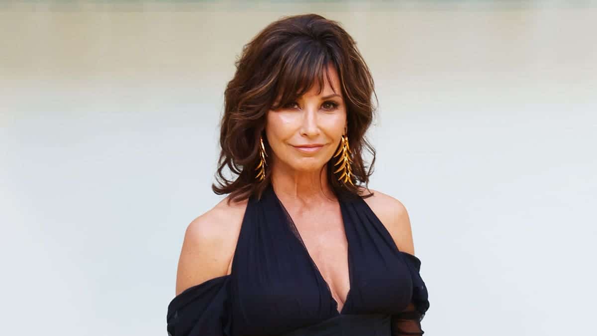 Gina Gershon wearing a low-cut black dress with gold earrings.