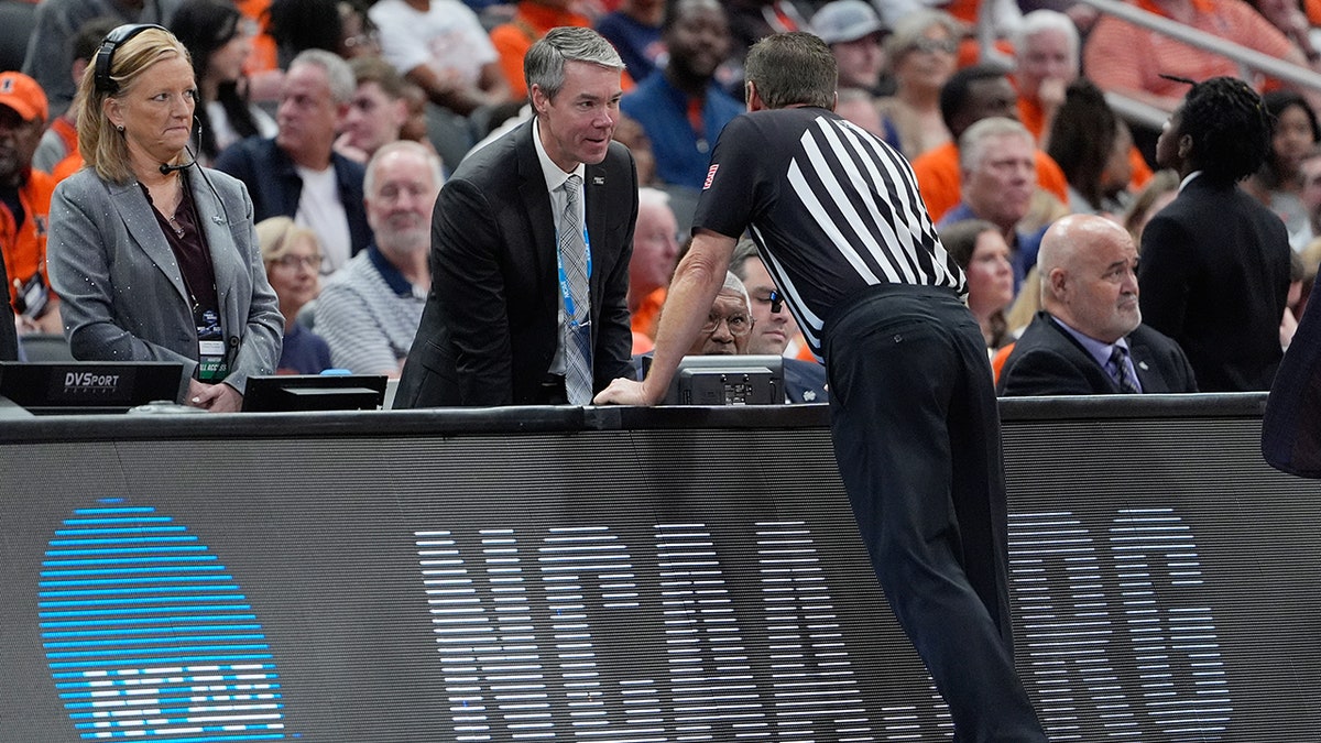 A referee talks with the scorer's table during a college basketball game