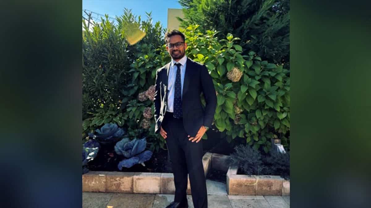 Tauhid Dewan stands in a suit smiling in front of a nature backdrop