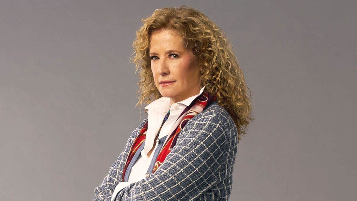Nancy Travis looking serious in a grey suit.
