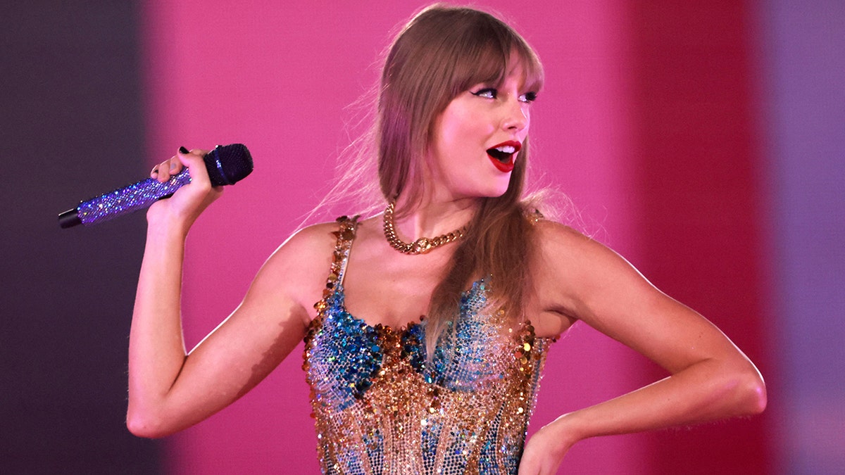 Taylor Swift standing and smiling in a pink outfit