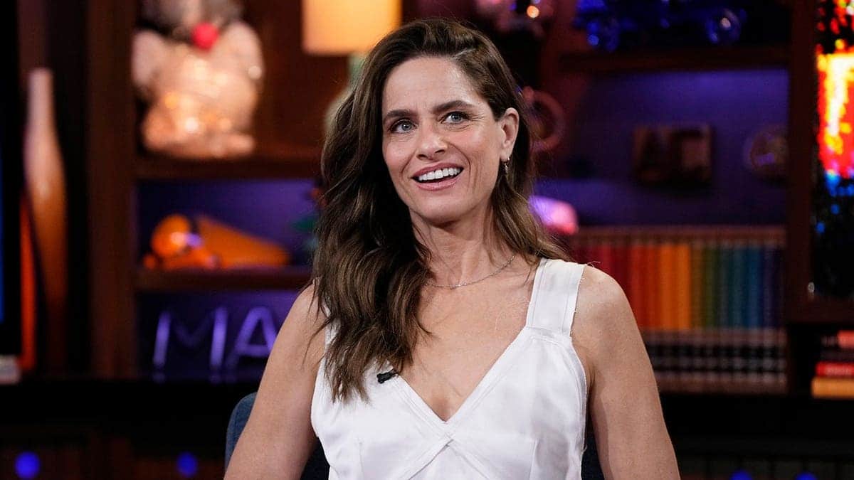 Amanda Peet smiling and seated on a television set