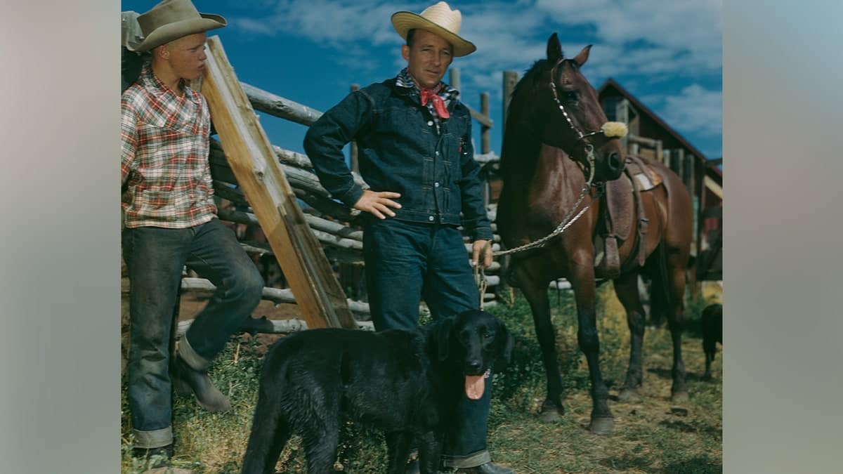 Bing Crosby standing against a fence with a horse and a dog in Nevada in 1950.