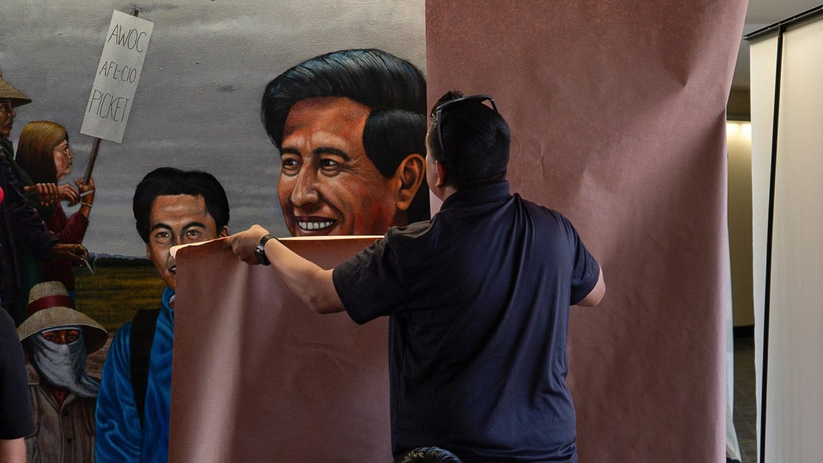 A worker covering a mural by Emigdio Vasquez depicting Cesar Chavez at Santa Ana College.