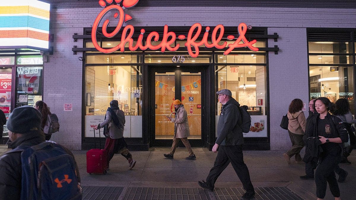 People walking in front of a Chick-fil-A restaurant with illuminated signage at night in Times Square New York City