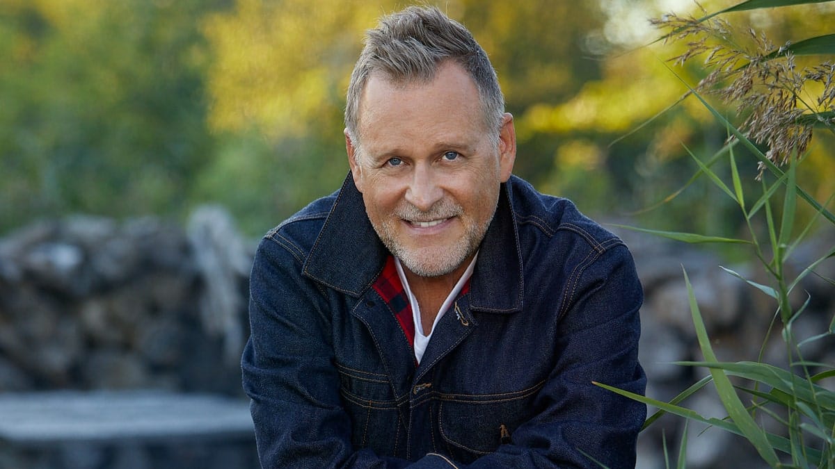 Dave Coulier sitting by a fire outdoors
