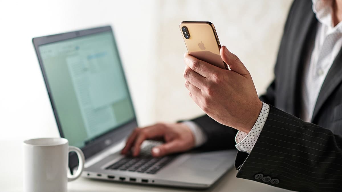 Person holding a smartphone while using a laptop