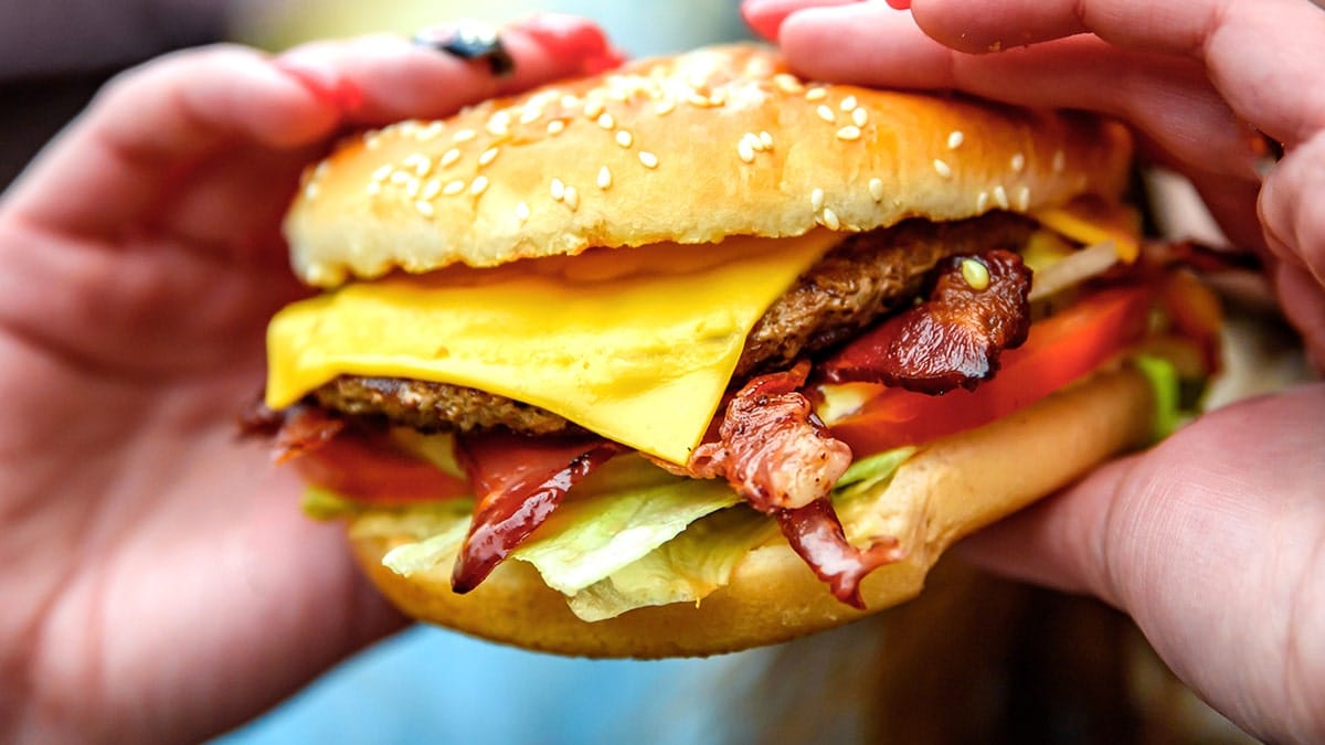 Person holding a bacon cheeseburger