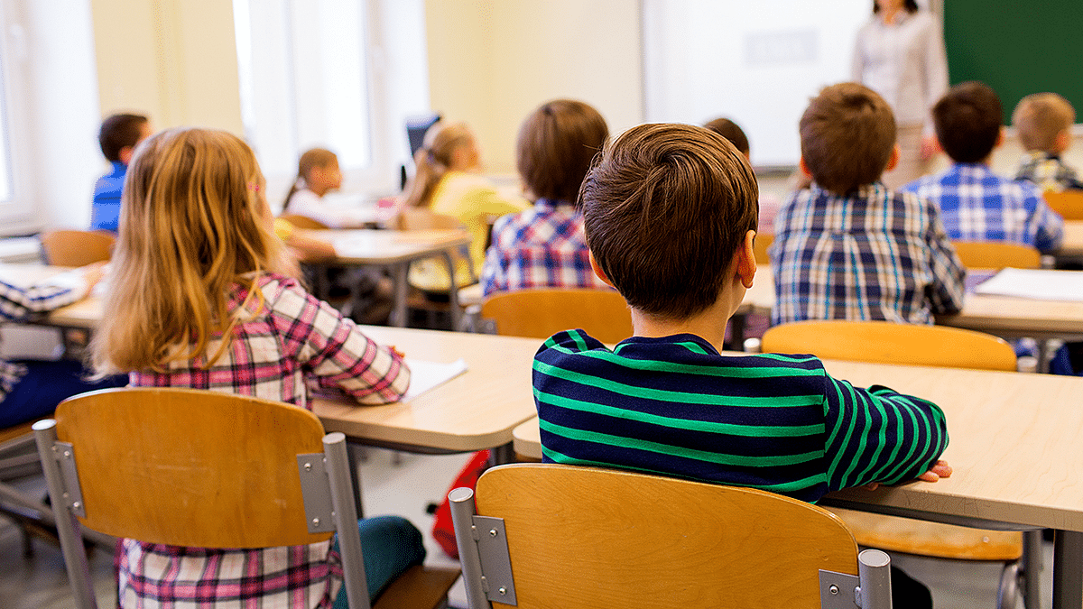Elementary school teacher standing in classroom with seated first-grade students