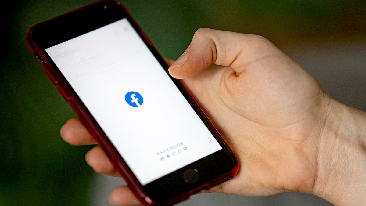 A person holds a phone with the Facebook logo on its screen.
