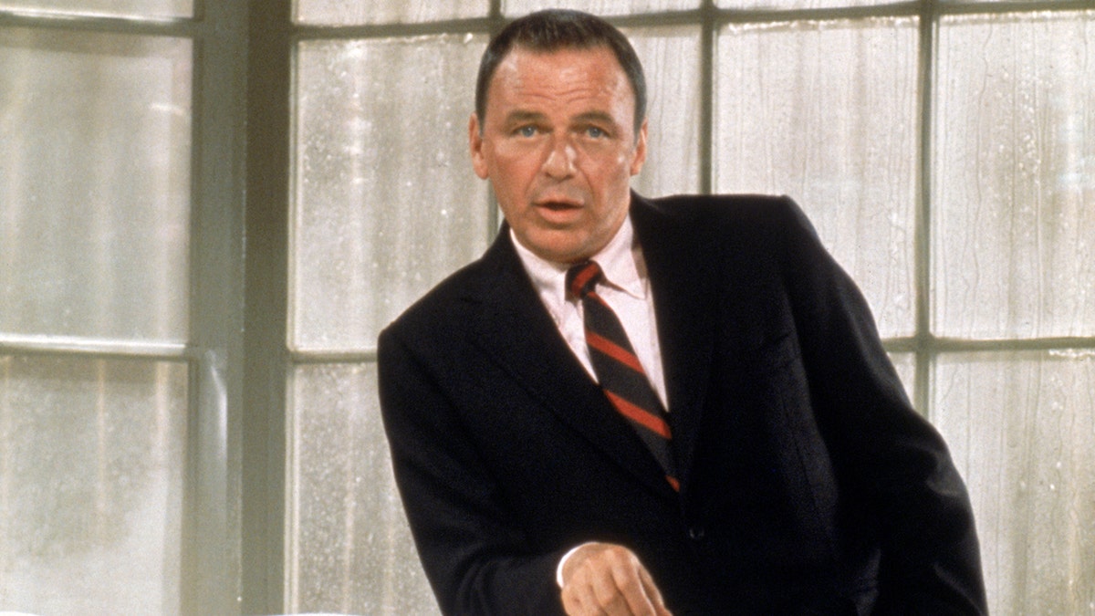 Frank Sinatra posing for a photo in a black suit in the 1960s.