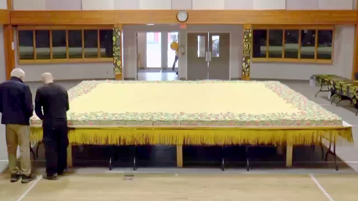 Two senior citizens are shown at the lower left of a giant carrot cake.
