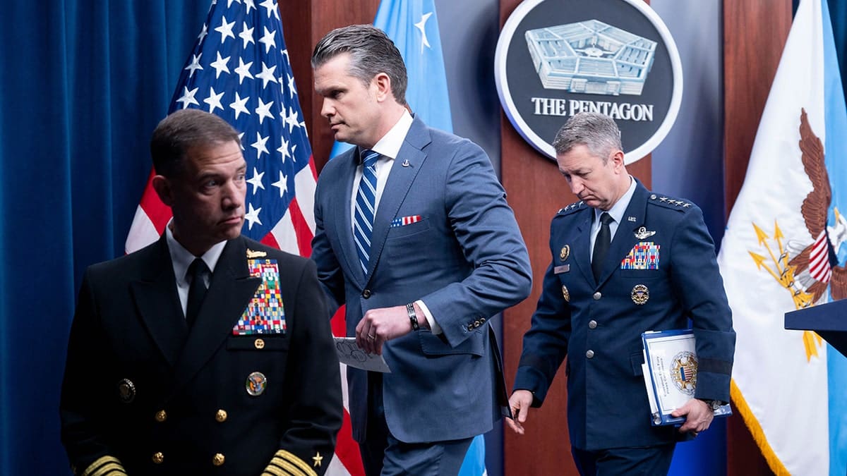 War Secretary Pete Hegseth walking away from podium with Gen. Dan Caine and Adm. Brad Cooper at Pentagon briefing