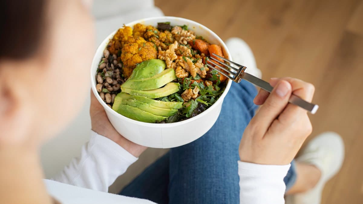 Woman eating fresh salad with avocado, beans, and vegetables.