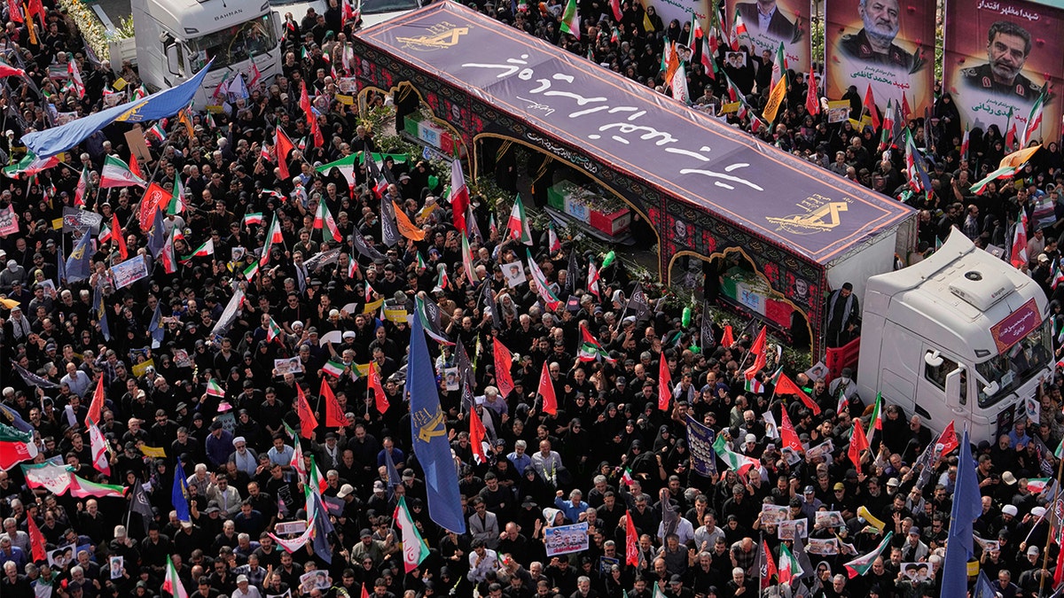 Mourners gather around flag-draped coffins on trucks during funeral ceremony in Tehran