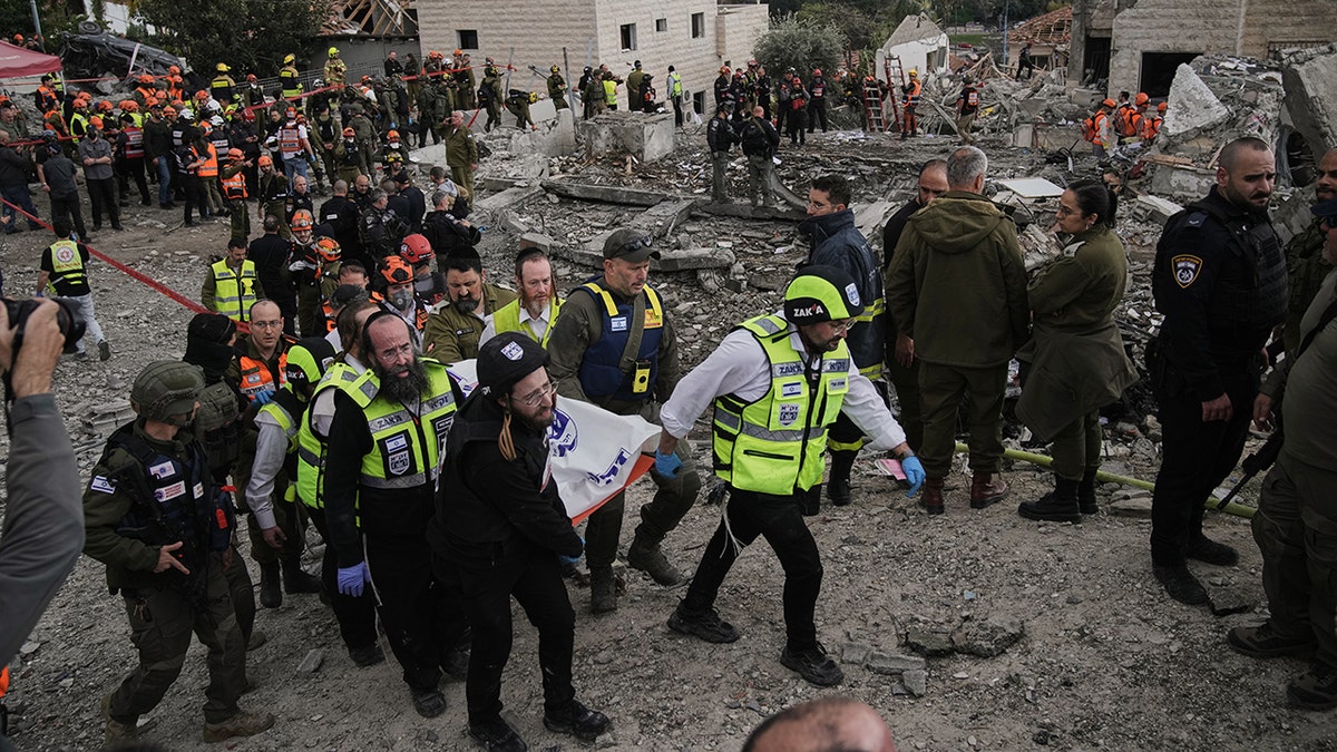 Rescue workers and military personnel carrying a body on a stretcher away from a debris-filled strike site.