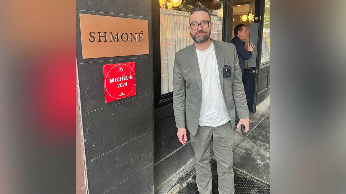 Fyksen standing outside Shmone restaurant in NYC, wearing suit and body cam, on Guinness World Record food tour of 28 Michelin-star restaurants.