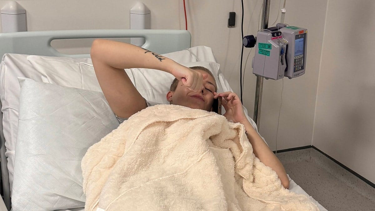 Kayley Boda lying in hospital bed with her phone up to her ear.