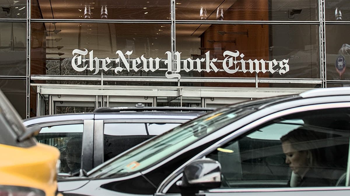The New York Times sign above the entrance to the newspaper's corporate headquarters in Times Square with cars and taxi cabs driving past.