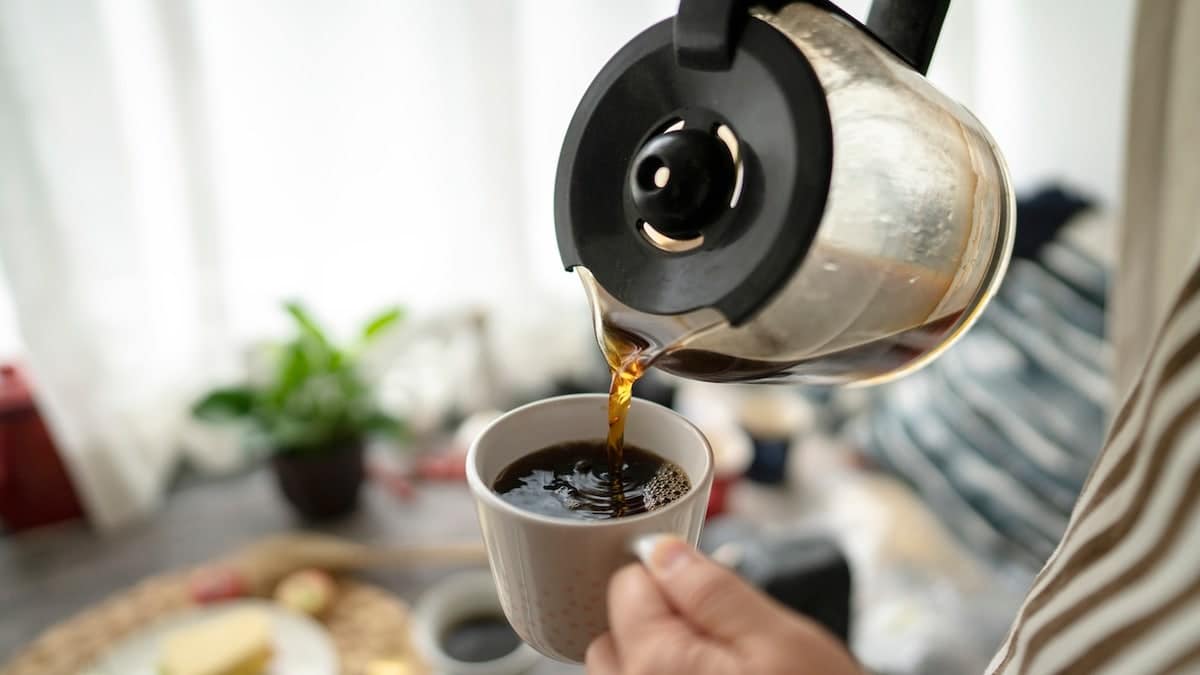Young woman pouring coffee into a mug in front of a window