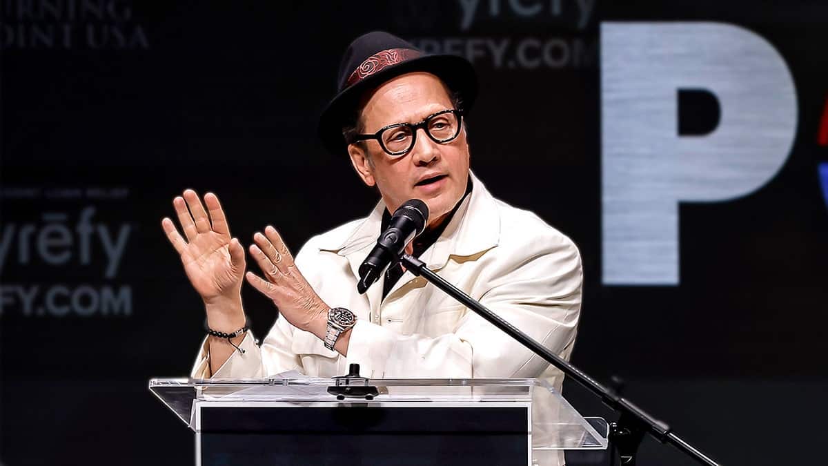 Comedian Rob Schneider speaking on stage at a Turning Point USA event at UC Berkeley