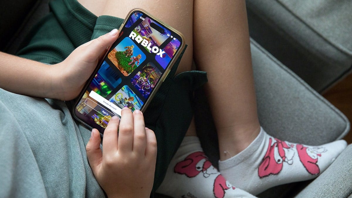 A child sitting on a couch playing Roblox on a smartphone.