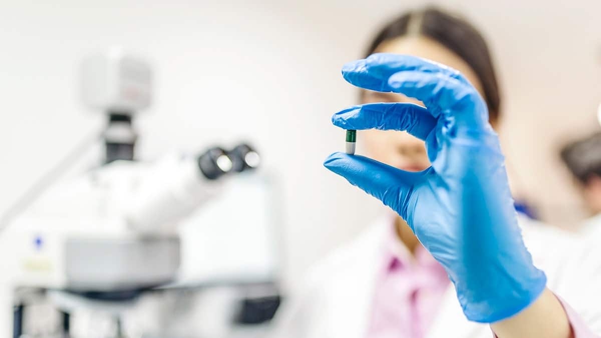 scientist in a lab holds up a blue and white pill