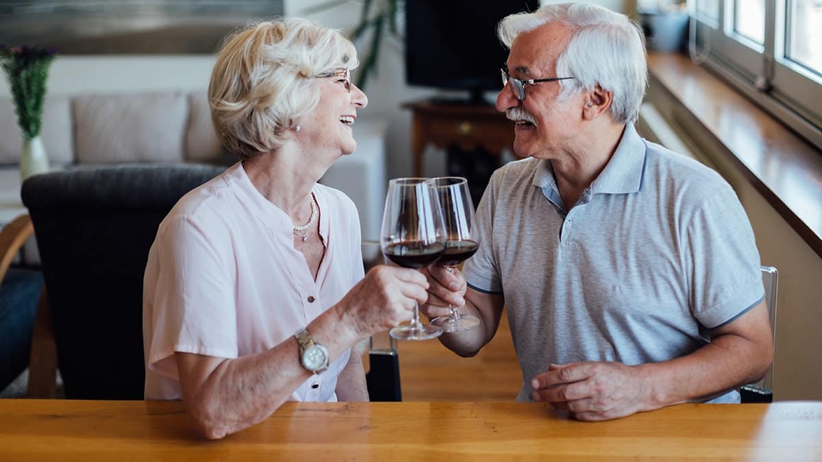 Happy senior couple enjoying a glass of red wine at home