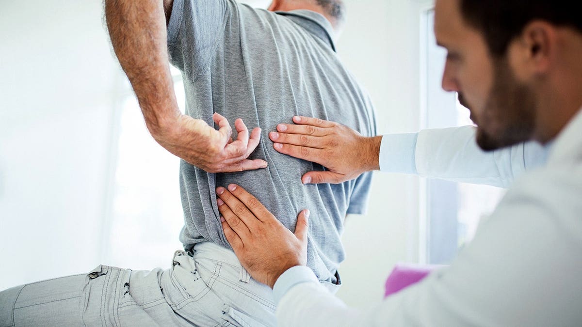 Senior man pointing to his lower back while sitting with a male doctor in a medical office