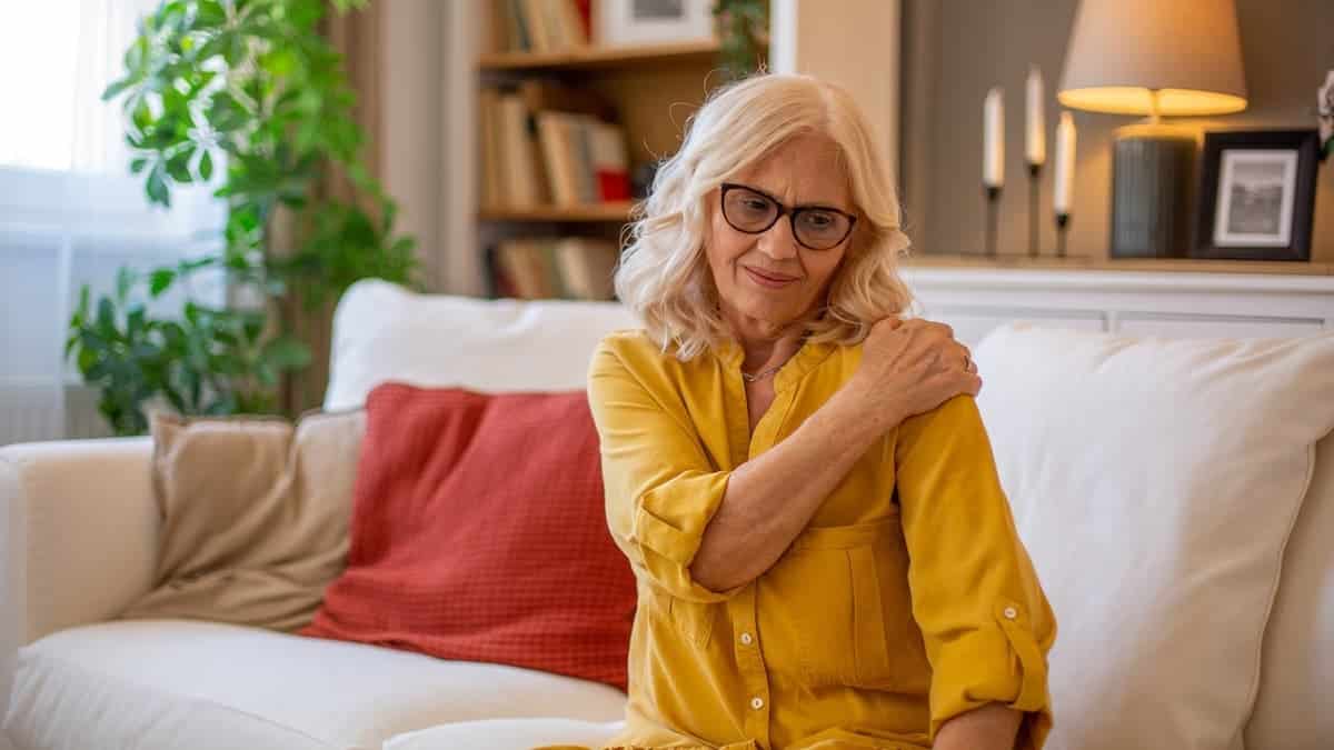 Senior woman massaging her shoulder while sitting on a sofa in a living room