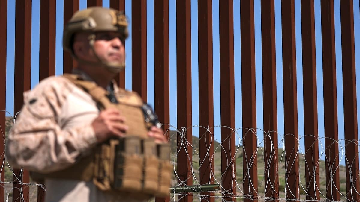 A Marine standing in front of concertina wire on a border wall in San Diego