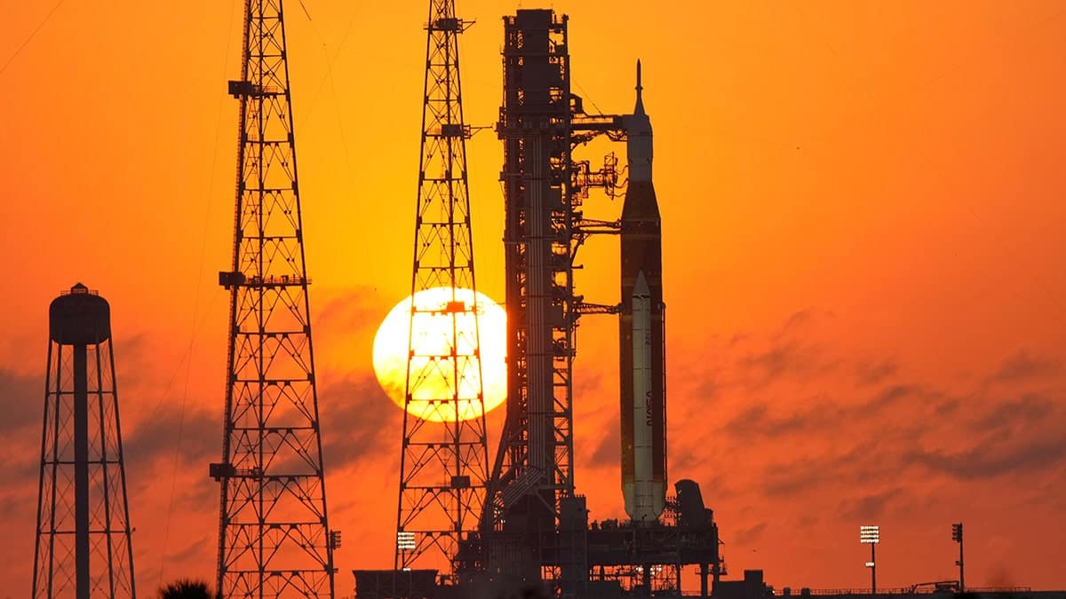 The NASA Space Launch System rocket and Orion spacecraft standing on a launch pad during a colorful sunrise.