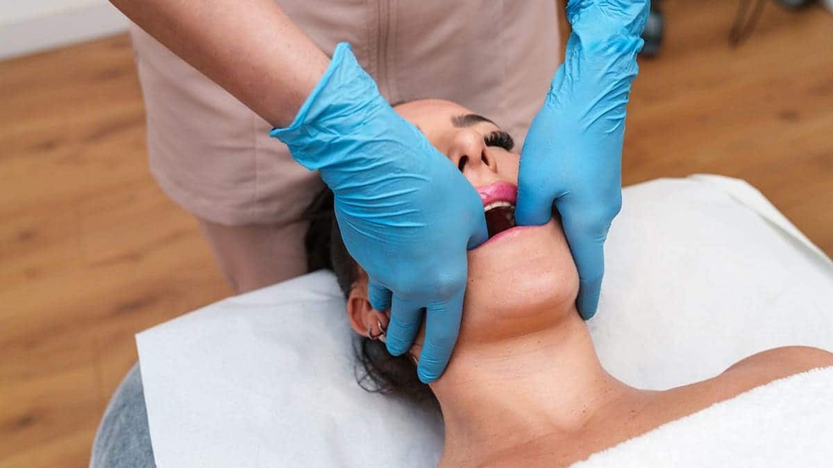 Therapist performing TMJ therapy on a relaxed patient's jawline