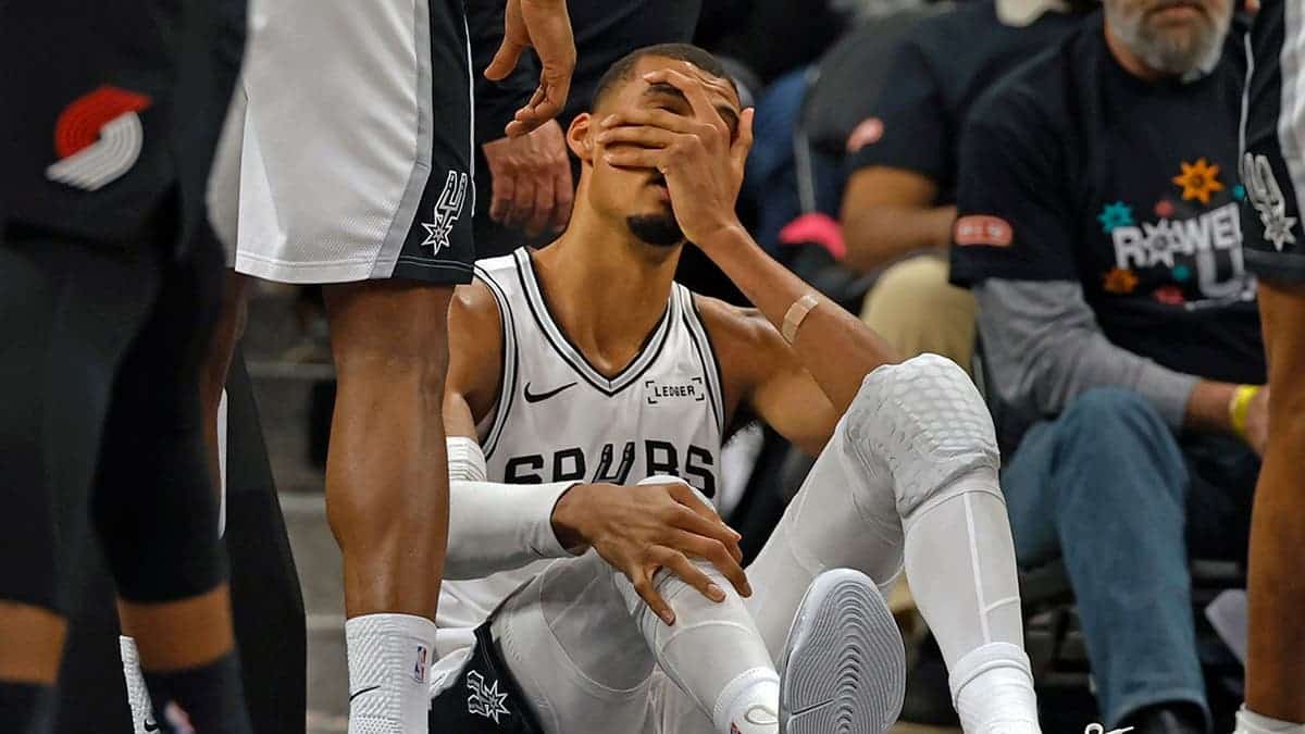 Victor Wembanyama holding his head after falling on the basketball court.
