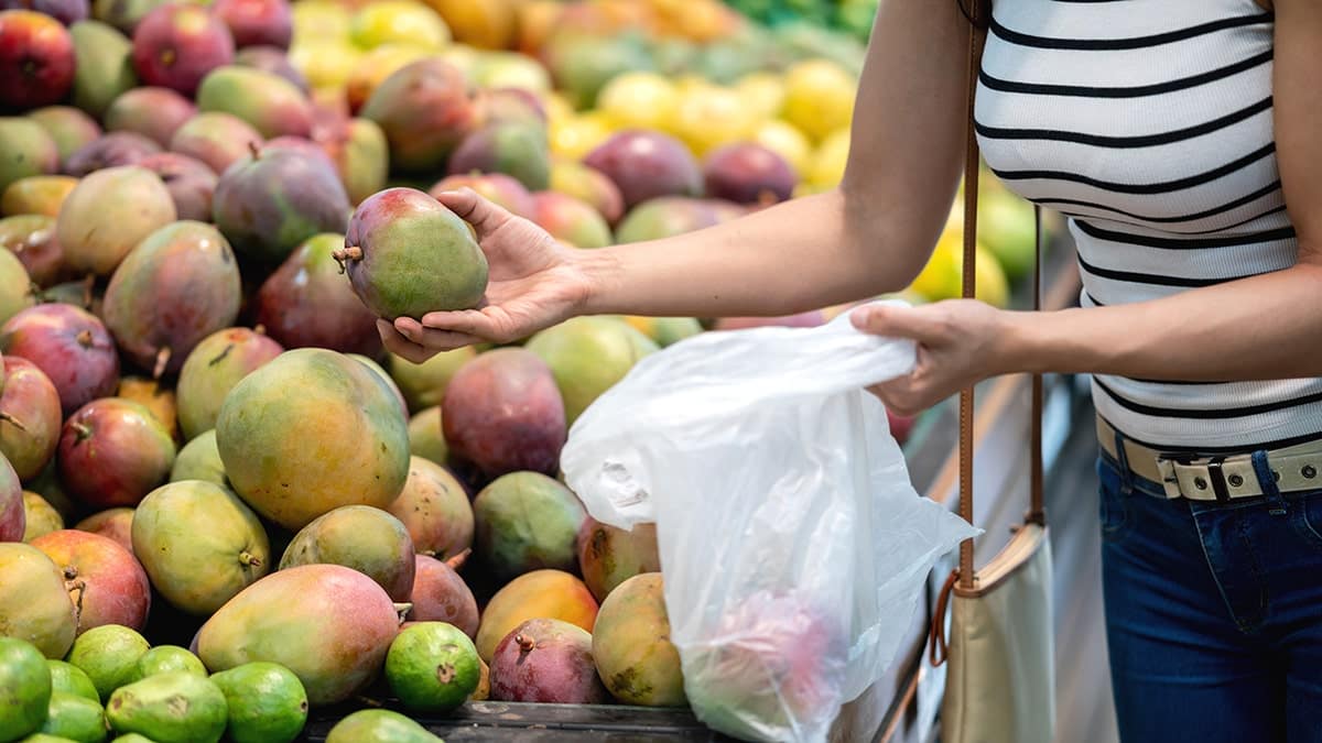 A woman holding mangoes in a supermarket while shopping