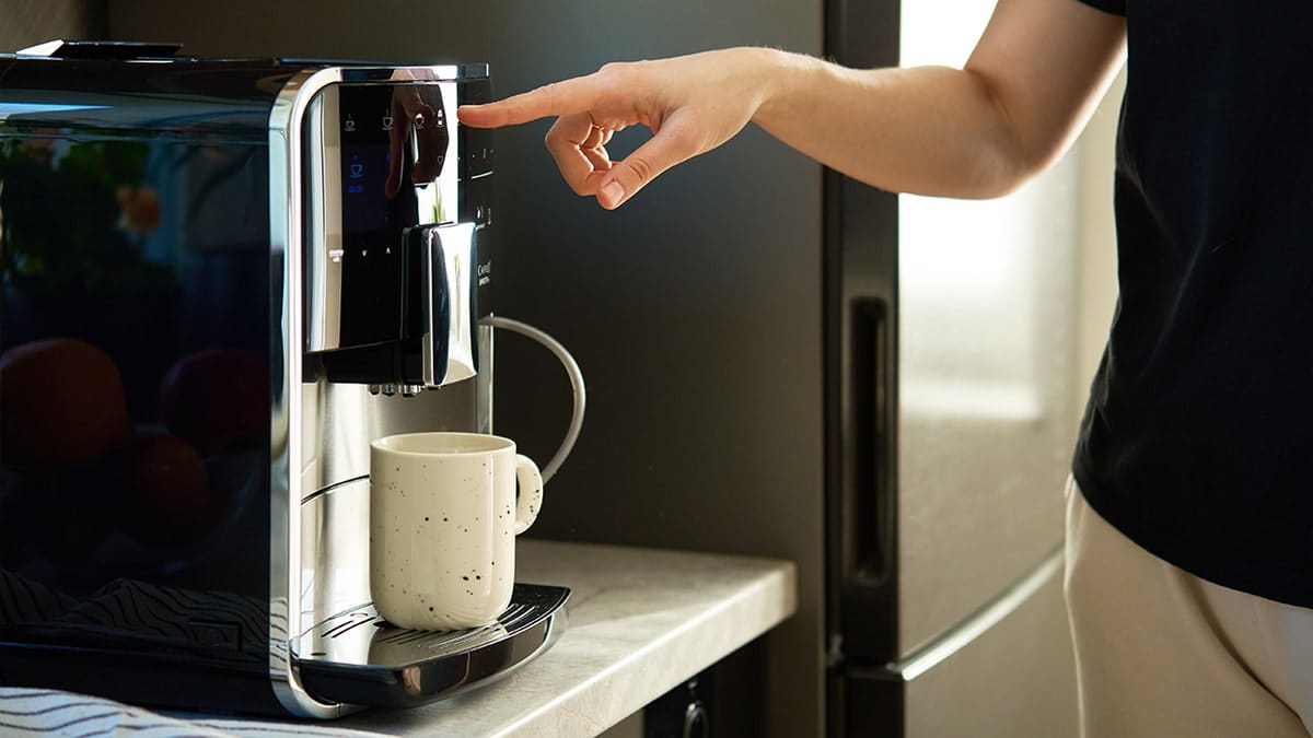 Woman pressing button on modern espresso machine with ceramic mug underneath