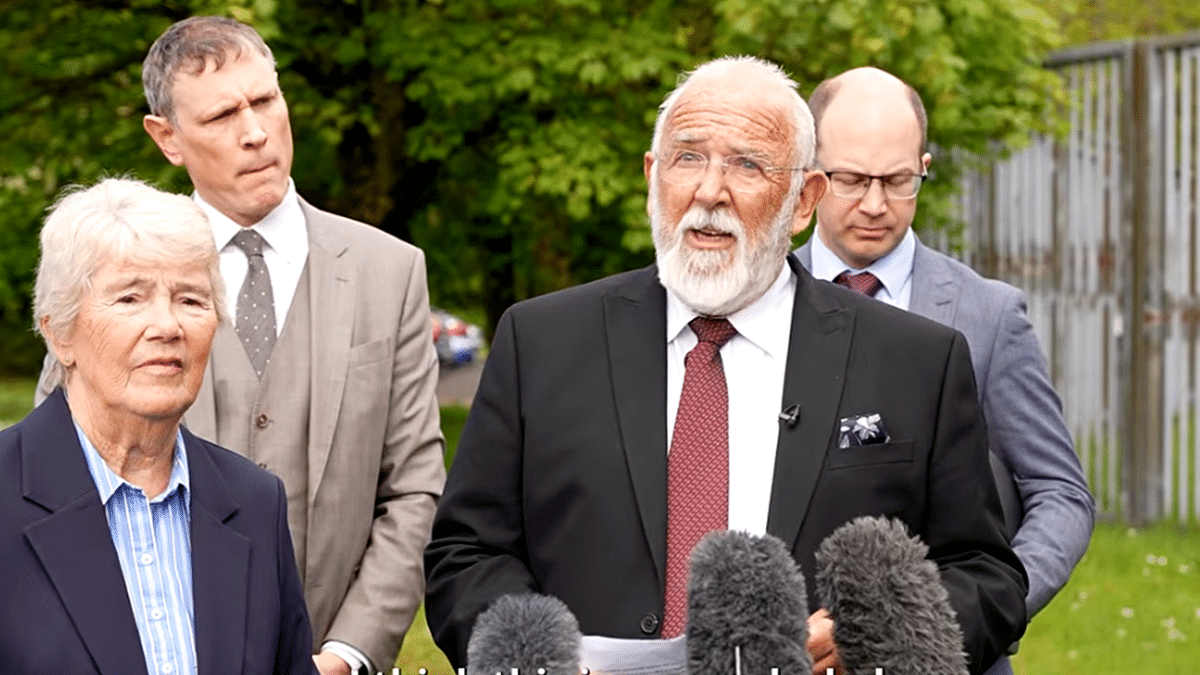 Retired pastor Clive Johnston at podium surrounded by family and legal team.