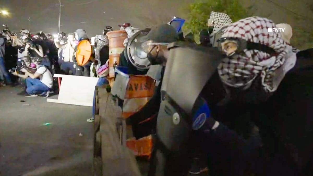 Protesters wearing goggles and keffiyehs hold makeshift shields during clashes with ICE agents.