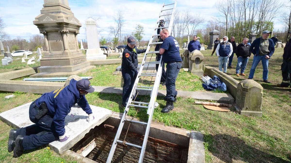 Police looking at an open crypt with a latter inside during their investigation at Mt. Moriah Cemetery.
