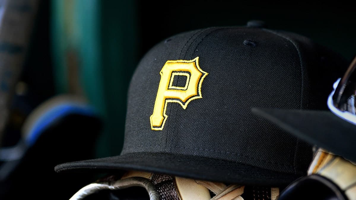 A New Era Pirates baseball hat with yellow P logo on a baseball glove on a dugout bench.