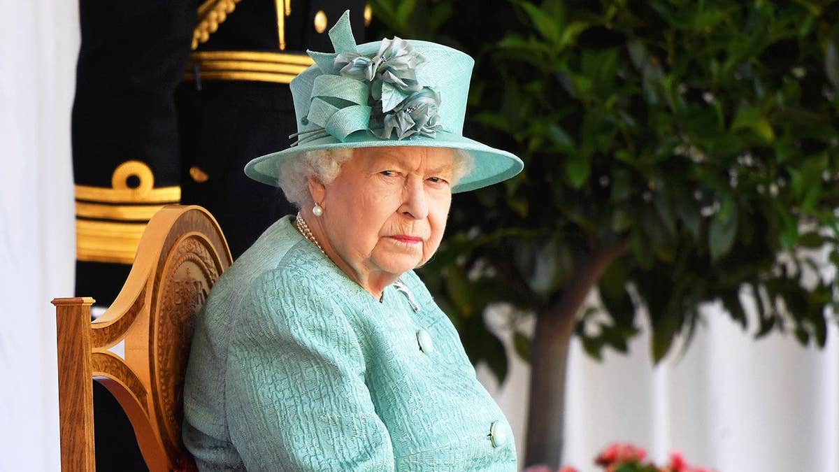 Queen Elizabeth II wearing a bright sky blue coat dress sitting on a golden chair with a matching hat.