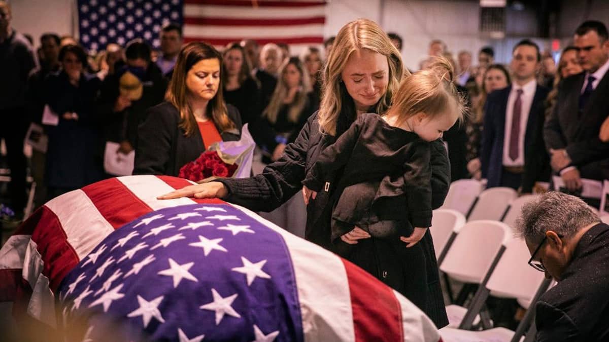 Amy King with her daughter, Adalyn. She has her hand on a casket of her late husband