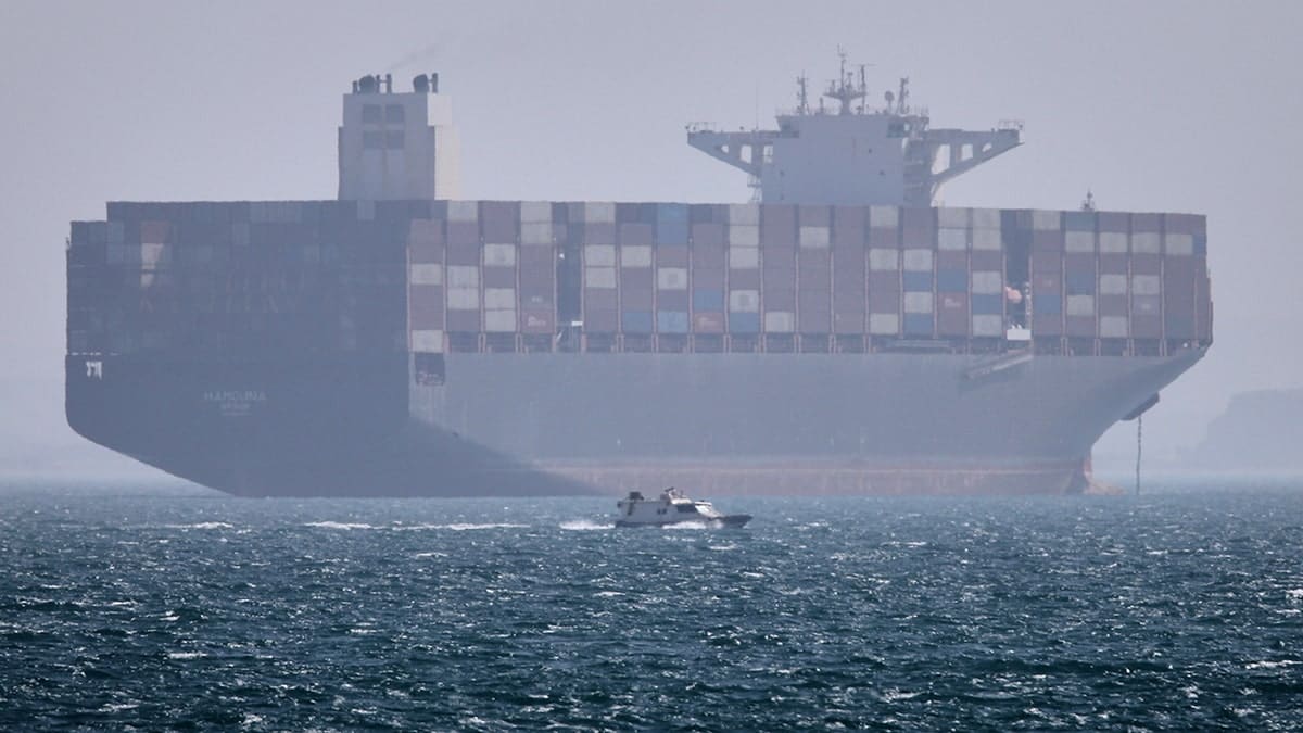 A container ship sitting at anchor in the Strait of Hormuz as a motorboat passes in the foreground