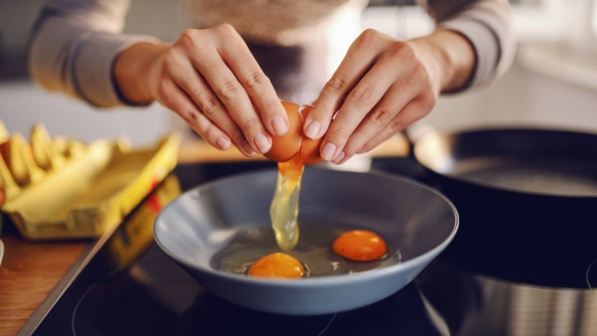 Hands cracking eggs into a pan to make sunny side up eggs.