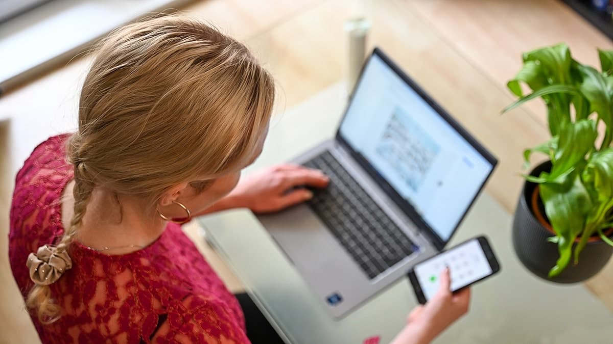 Woman typing on laptop and phone at desk