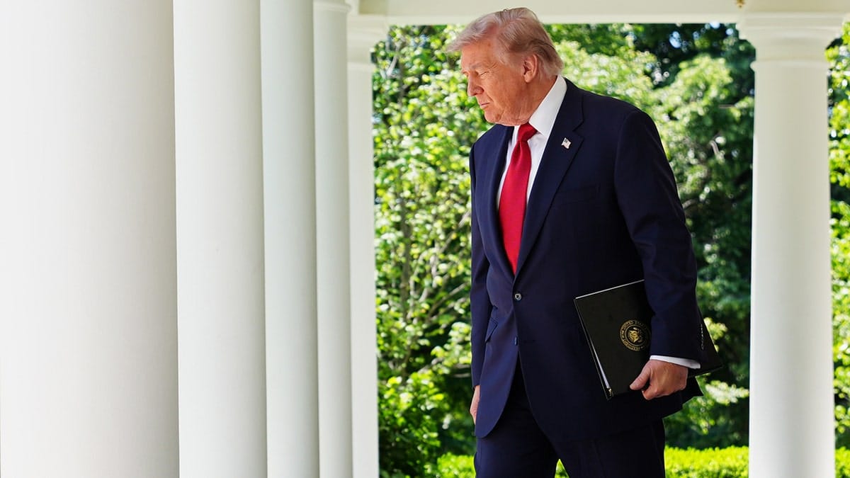 Donald Trump walks through the White House Colonnade while holding a black folder.