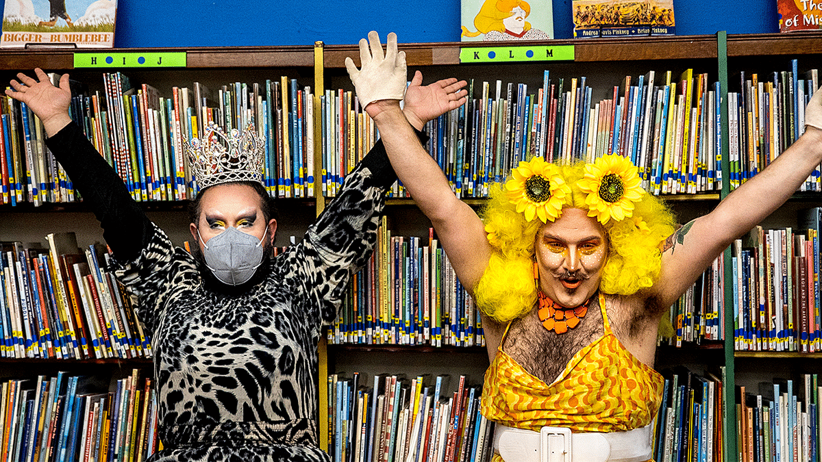 Drag queens raise their arms in front of books in library