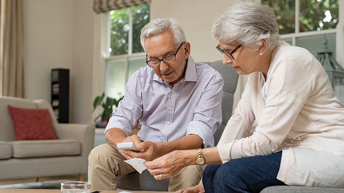 An elderly couple sitting together calculating a receipt.