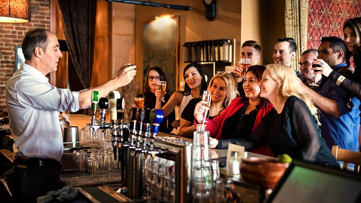 People cheering at a bar counter while bartender takes a picture on mobile phone